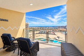 Ein Balkon mit Blick auf Strand und Pool, zwei Korbstühle und eine Wand mit Fliesen in Zickzackmuster.
