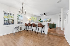A modern kitchen with a bar area, wooden flooring, and a ceiling fan. - 4BR Home with Pool and Firepit Near SanTan Village (Gilbert)