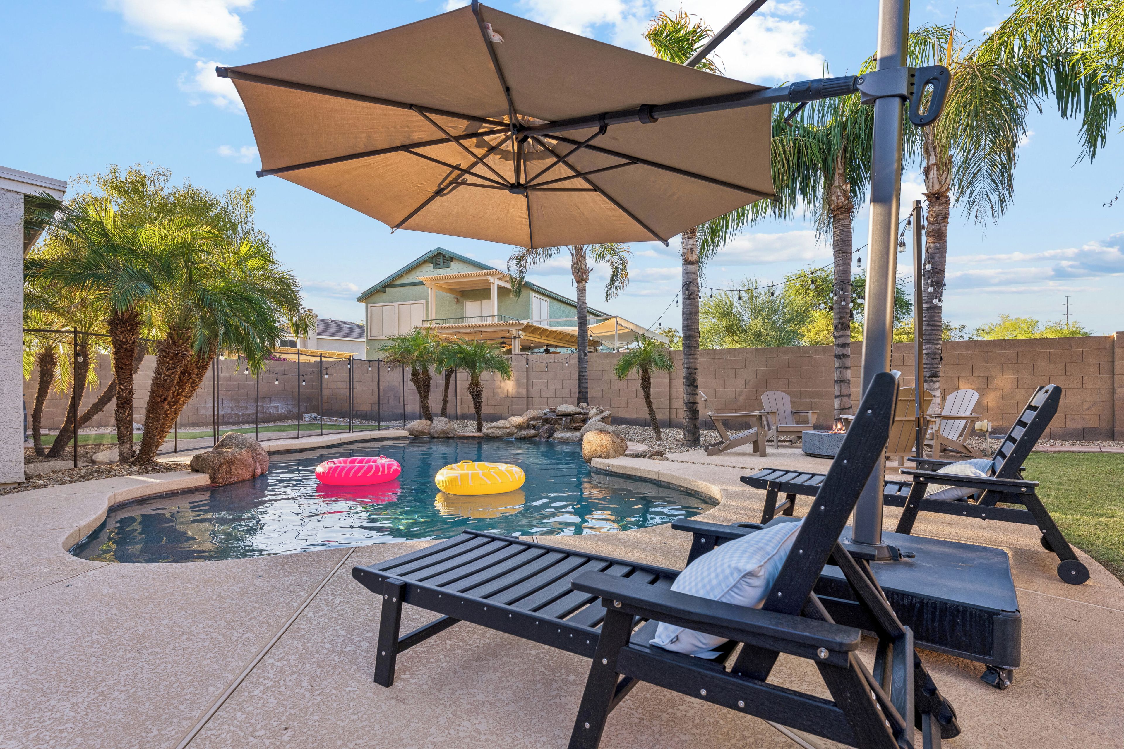 A backyard with a swimming pool, lounge chairs, and an umbrella.
