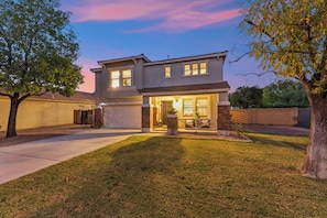 A two-story residential house with a front porch, a garage, and a well-maintained lawn. - 4BR Home with Pool and Firepit Near SanTan Village (Gilbert)