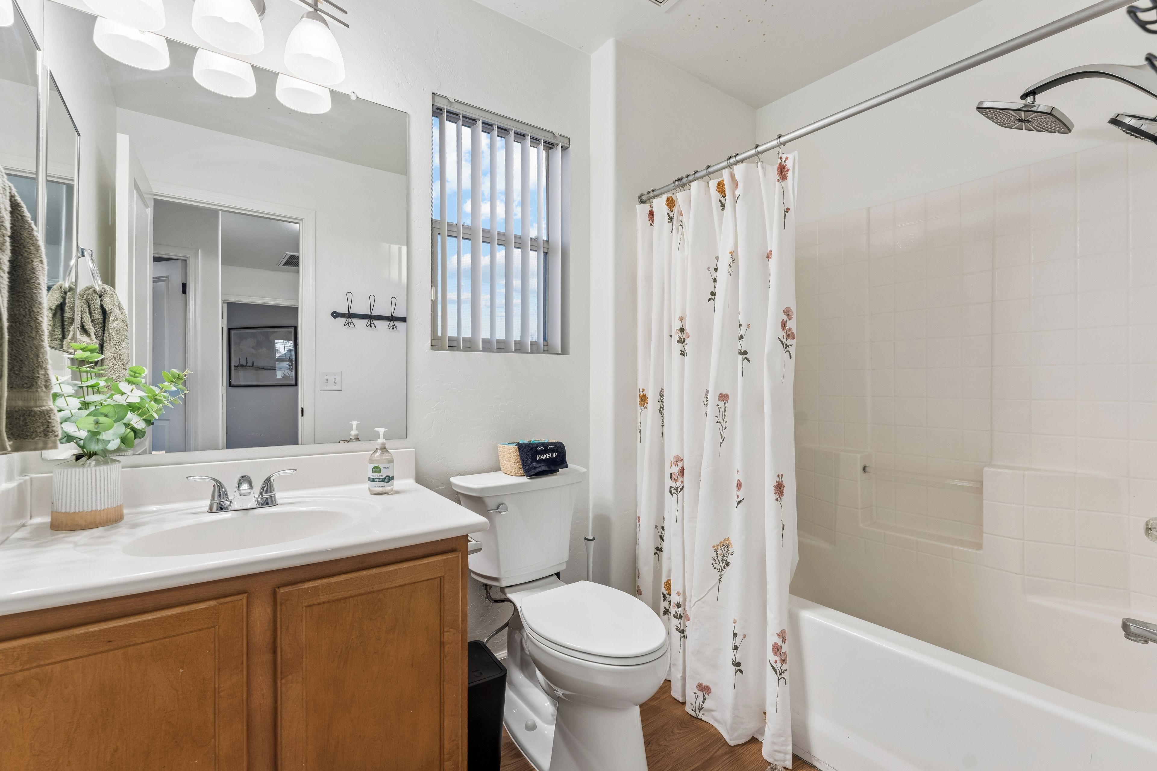 A bathroom with a white sink, a toilet, a shower with a glass door, and a window with vertical blinds.
