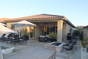 Eine Terrasse mit Liegestühlen, Sonnenschirmen und einem Grill.