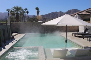 Ein Pool mit Whirlpool, Liegestühlen und einem weißen Sonnenschirm.