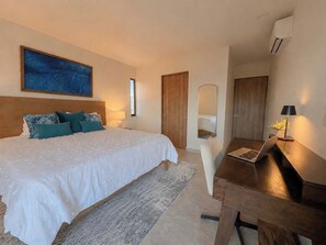 Une chambre à coucher avec un lit, un bureau avec un ordinateur portable, un miroir et un tableau accroché au mur.