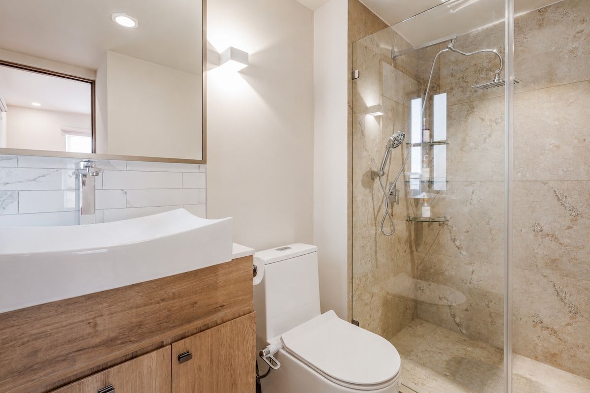 Une salle de bain moderne avec une douche à parois de verre, des toilettes blanches et un meuble-lavabo en bois.