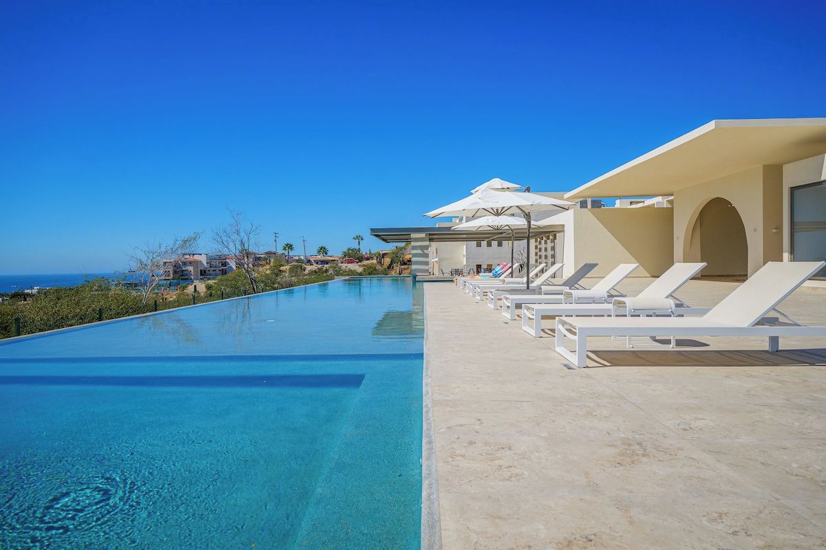 A swimming pool with lounge chairs and umbrellas, overlooking a coastal area.