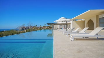 A swimming pool with lounge chairs and umbrellas, overlooking a coastal area.