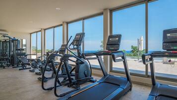 A gym with treadmills and exercise equipment, large windows, and a view of the sea.