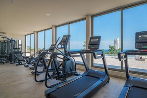 Une salle de sport équipée de tapis de course et d’appareils d’exercice, dotée de grandes fenêtres et offrant une vue sur la mer.