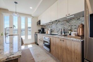 Une cuisine moderne dotée d’un grand îlot central, d’appareils électroménagers en acier inoxydable et offrant une vue sur l’extérieur.