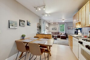 Een moderne keuken met houten kasten, een eethoek met tafel en stoelen, en een woonkamer met een bank en salontafel.