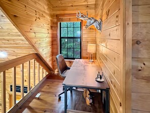 Ein Holzblockhaus-Interieur mit Esstisch, Stuhl, Lampe und einem an der Wand befestigten Hirschkopf.