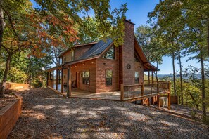 A wooden cabin with a deck, surrounded by trees and a gravel driveway. - Peaceful Peaks - Mountain View | Hot Tub | Pet Friendly | Game Room | Firepit (Mineral Bluff)