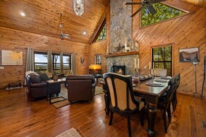 A spacious living area with a fireplace, wooden flooring, and large windows offering a view of the outdoors. - Peaceful Peaks - Mountain View | Hot Tub | Pet Friendly | Game Room | Firepit (Mineral Bluff)