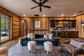 A cozy living room with a dark blue sofa, two fluffy white dogs, and a wooden interior. - Blue Mountain Retreat - Panoramic Mountain Views | Gourmet Kitchen | Expansive Decks | Dogs OK (Morganton)