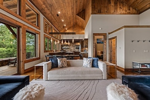 A spacious living area with a large sofa, a dining table, and a kitchen in the background. - Blue Mountain Retreat - Panoramic Mountain Views | Gourmet Kitchen | Expansive Decks | Dogs OK (Morganton)