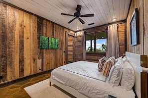 A bedroom with a wooden wall, a ceiling fan, a bed with white bedding, and a window with curtains. - Blue Mountain Retreat - Panoramic Mountain Views | Gourmet Kitchen | Expansive Decks | Dogs OK (Morganton)