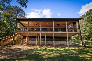 Eine zweistöckige Holzhütte mit Steinfundament, einer Treppe links und einem Balkon im oberen Geschoss.