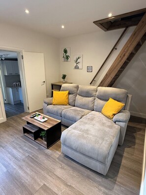 A living room with a grey sofa, a coffee table, and a staircase. - Large Private Suite for Families & Workers Near Hospital (Greater London)
