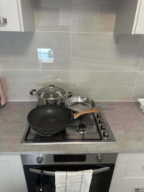 Een keuken met een gasfornuis, een koekenpan, een pan en een braadpan op het aanrecht.