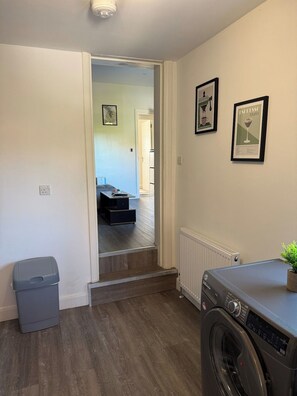 A laundry room with a washing machine, a trash bin, and a radiator. - Large Private Suite for Families & Workers Near Hospital (Greater London)