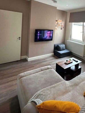 A living room with a sofa, a coffee table, a television, and a window. - Large Private Suite for Families & Workers Near Hospital (Greater London)