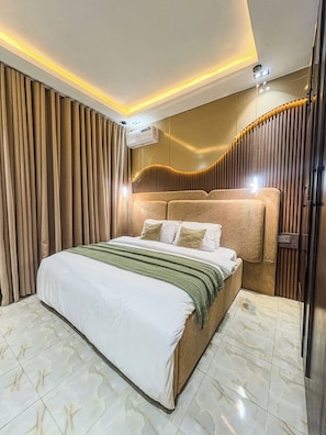 A modern hotel room with a large bed, a built-in headboard, and a wall-mounted air conditioning unit. - Swan Luxury Homes | Luxury 2-Bedroom Shortlet Apartment, Wuye, Abuja (Abuja)