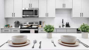 A modern kitchen with white cabinets, a microwave, oven, and two potted plants on the counter.