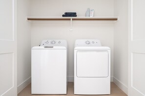 A laundry room with two white washing machines and a shelf above them. - Modern WorkerFriendly Lndry, GYM & Pool (Sherman)