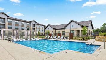 A swimming pool with lounge chairs and a building with multiple floors and balconies.
