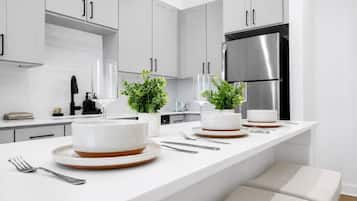 Une cuisine moderne avec des meubles blancs, un réfrigérateur en acier inoxydable et un grand îlot central agrémenté d’assiettes et de bols blancs.