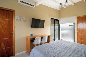 A bedroom with a bed, a desk with two chairs, a television, and a sliding glass door.