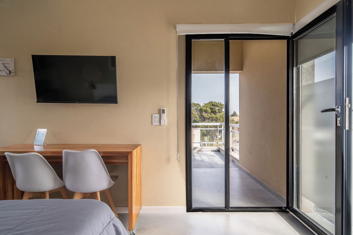 Ein Hotelzimmer mit einem Bett, einem Schreibtisch mit zwei Stühlen, einem Fernseher und einer Glastür zu einem Außenbereich.