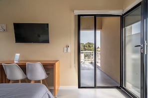 Ein Hotelzimmer mit einem Bett, einem Schreibtisch mit zwei Stühlen, einem Fernseher und einer Glastür zu einem Außenbereich.