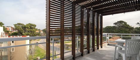 A covered outdoor area with a pergola structure, a table with chairs, and a view of the surrounding neighborhood.