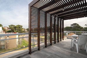 Ein überdachter Außenbereich mit einer Pergola, einem Tisch mit Stühlen und Blick auf die umliegende Nachbarschaft.