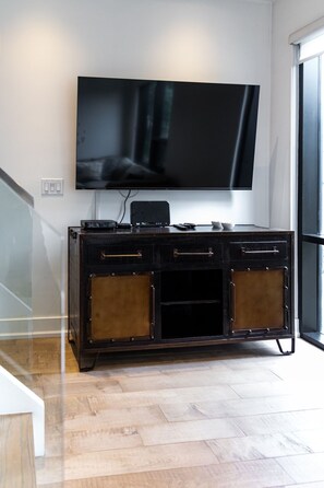 Ein modernes Wohnzimmer mit einem flachbildfernseher an der Wand, einer dunkelholzigen Unterhaltungsanlage mit Schubladen und einem Holzboden mit Fischgrätmuster.
