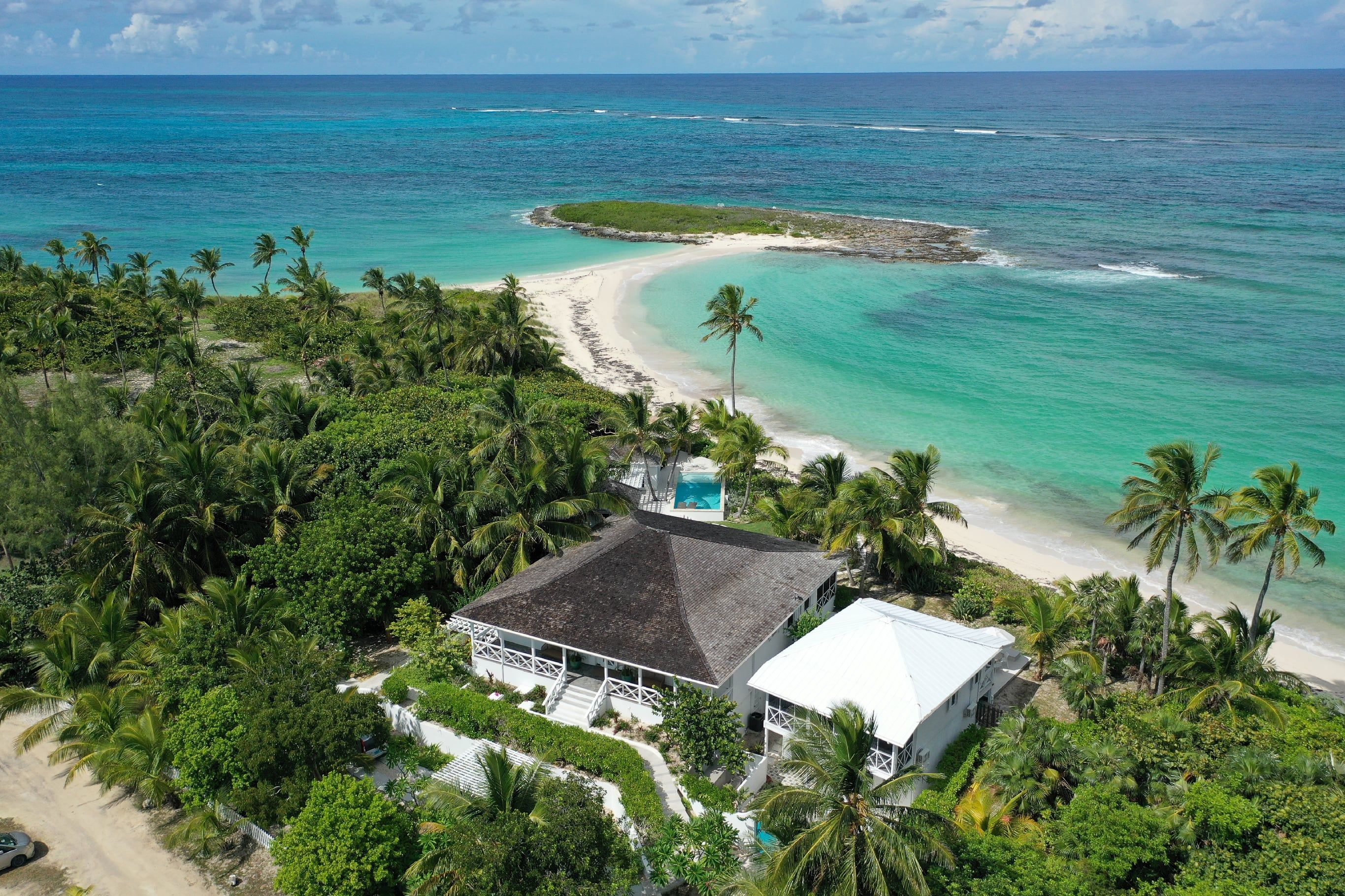 A beachfront property with a white building, a swimming pool, and a view of the ocean.