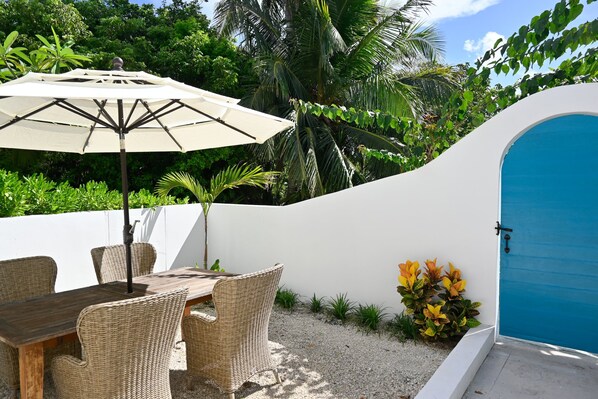 An outdoor seating area with wicker furniture and a table, a white wall, and a blue door. - Private Estate with Pool & Two Pickleball Courts Directly on Twin Coves Beach (Governor's Harbour)