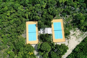 An aerial view of a property with two adjacent tennis courts surrounded by dense greenery. - Private Estate with Pool & Two Pickleball Courts Directly on Twin Coves Beach (Governor's Harbour)