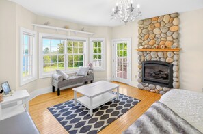 A living room with a stone fireplace, a grey sofa, and a chandelier. - Spacious 5-bedroom house with Hot Tub, Sauna, Steam Room, Bar, Gym,& Family Fun (Michigamme)