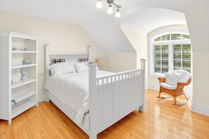 A bedroom with a white bed, a white wardrobe, a wicker chair, and a large window. - Spacious 5-bedroom house with Hot Tub, Sauna, Steam Room, Bar, Gym,& Family Fun (Michigamme)
