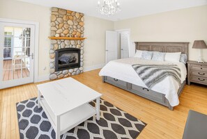 Une chambre avec une cheminée en pierre, un lit avec une tête de lit en bois, une table de chevet et une table blanche.