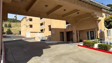 Un edificio con zona de estacionamiento techada, acceso para sillas de ruedas y bordillo rojo.