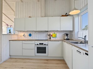 Una cuina moderna amb armaris blancs, taulell de fusta i forn de sobreencastrat.