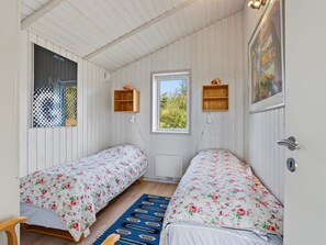 Una habitació amb dos llits individuals, una finestra, un radiador i una porta amb mànecs.