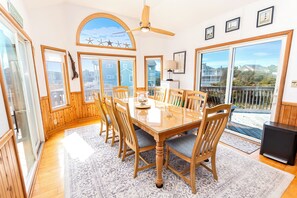 A dining room with a glass table and wooden chairs, large windows, and a view of buildings. - Semi-Oceanfront- Private Pool, Hot Tub-OH1200, Spyglass (Corolla)