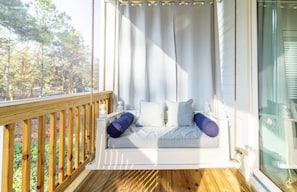 Une terrasse en bois avec un fauteuil suspendu et une vue sur les arbres.