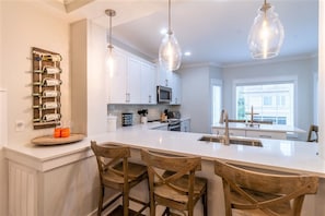 A kitchen with a central island, wooden chairs, pendant lights, and a wine rack. - Free 6-Seat Golf Cart | Private Free Heated Pool | Walk to Beach | Sleeps 18 (Hilton Head Island)