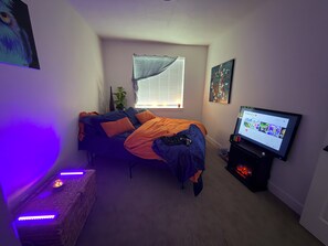 Ein Schlafzimmer mit einem Bett, einem Fernseher, einem Fenster mit Jalousien und einem Wandregal.